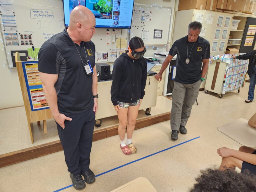 Officers showing the students the standardized field sobriety test while wearing the drunk goggles.