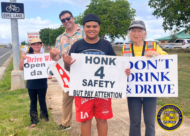 HPD officers and community members standing roadside hold signs promoting traffic safety