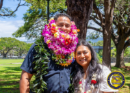 HPD officer with leis adorned his neck posing next to a woman
