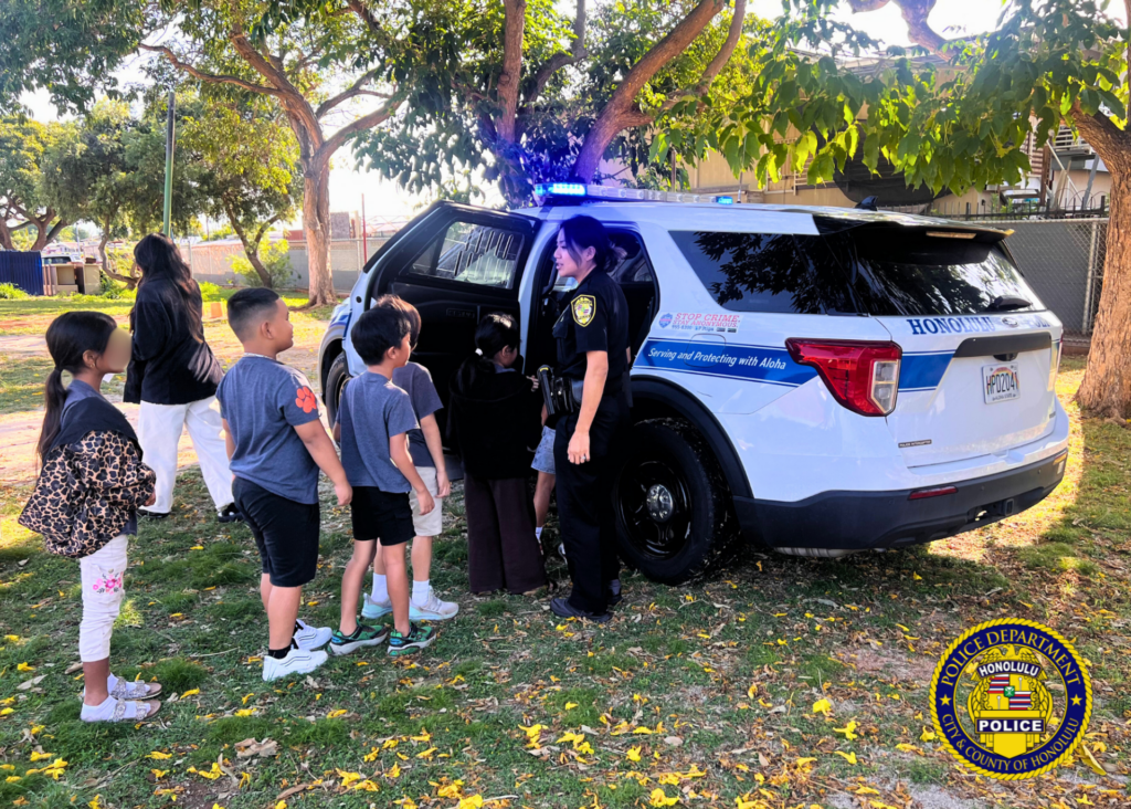 HPD officer at the opening to a police vehicle and children exploring the vehicle