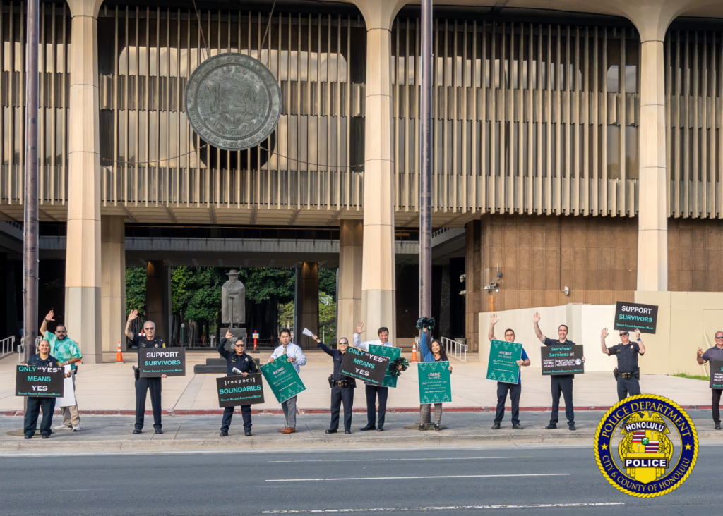 In front of the Hawaii State Capitol, HPD officers in uniform and community members holding signs in observance of Sexual Assault Awareness Month.