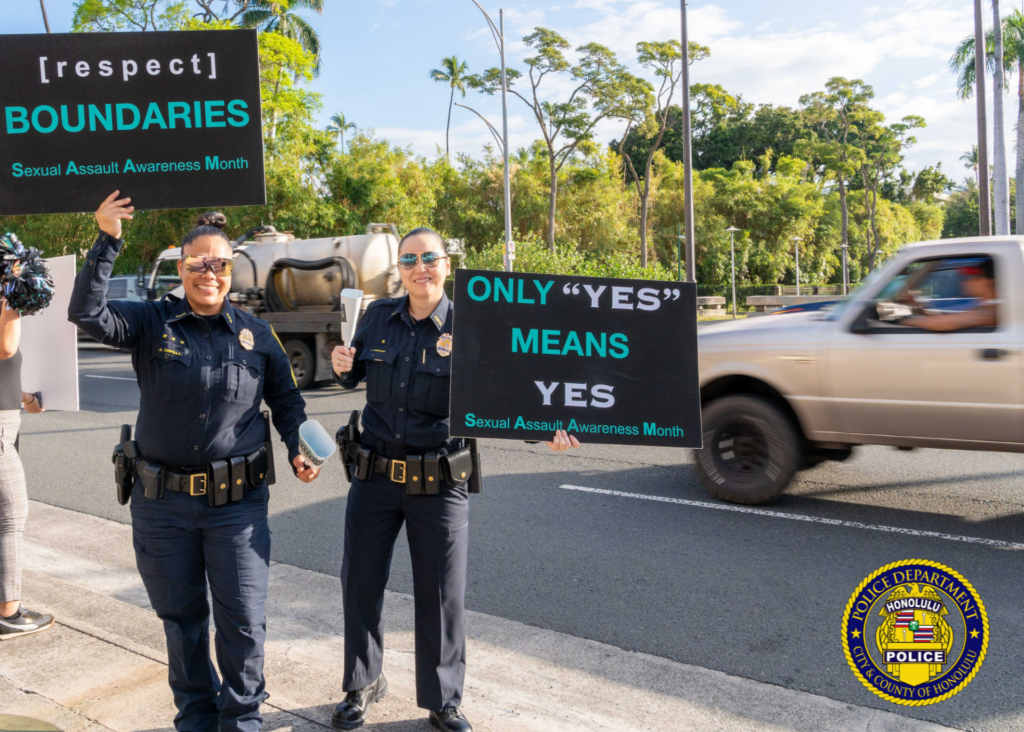 In front of the Hawaii State Capitol, two HPD officers in uniform holding signs in observance of Sexual Assault Awareness Month.
