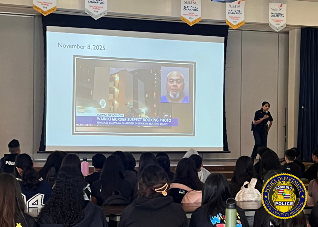 A Honolulu Police Department officer speaks to students while a presentation is displayed on a projector.