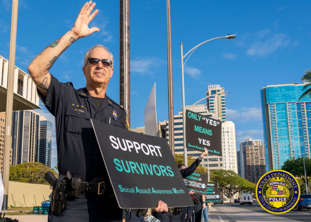 In front of the Hawaii State Capitol, one HPD officer in uniform holding signs in observance of Sexual Assault Awareness Month and waving the passerbys.