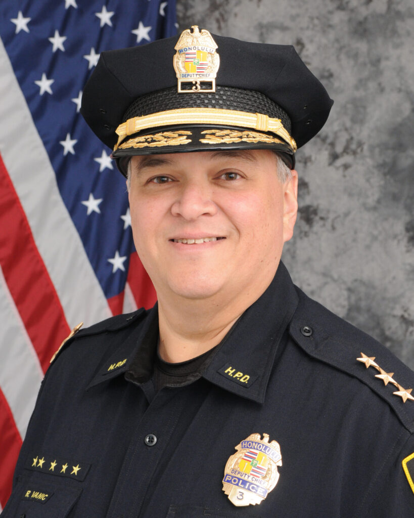 A portrait-style photograph of Rade Vanic, the Interim Chief of Police for the Honolulu Police Department. He is dressed in uniform with a police hat, and the Hawaiian flag is visible in the background. A portrait-style photograph of Rade Vanic, the Interim Chief of Police for the Honolulu Police Department. He is dressed in uniform with a police hat, and the Hawaiian flag is visible in the background.