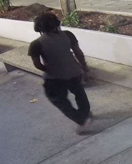 Unknown male suspect possibly wearing a gold watch or bracelet on his left wrist, long pants, and a t-shirt under a tank top as shown on surveillance camera